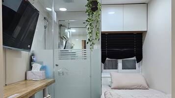 A compact bedroom with a bed, a desk, a chair, and a TV.