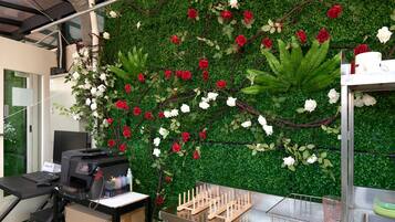 Un espacio de trabajo con una pared verde decorada con flores rojas y blancas, una impresora y una mesa metálica con un recipiente de vidrio.