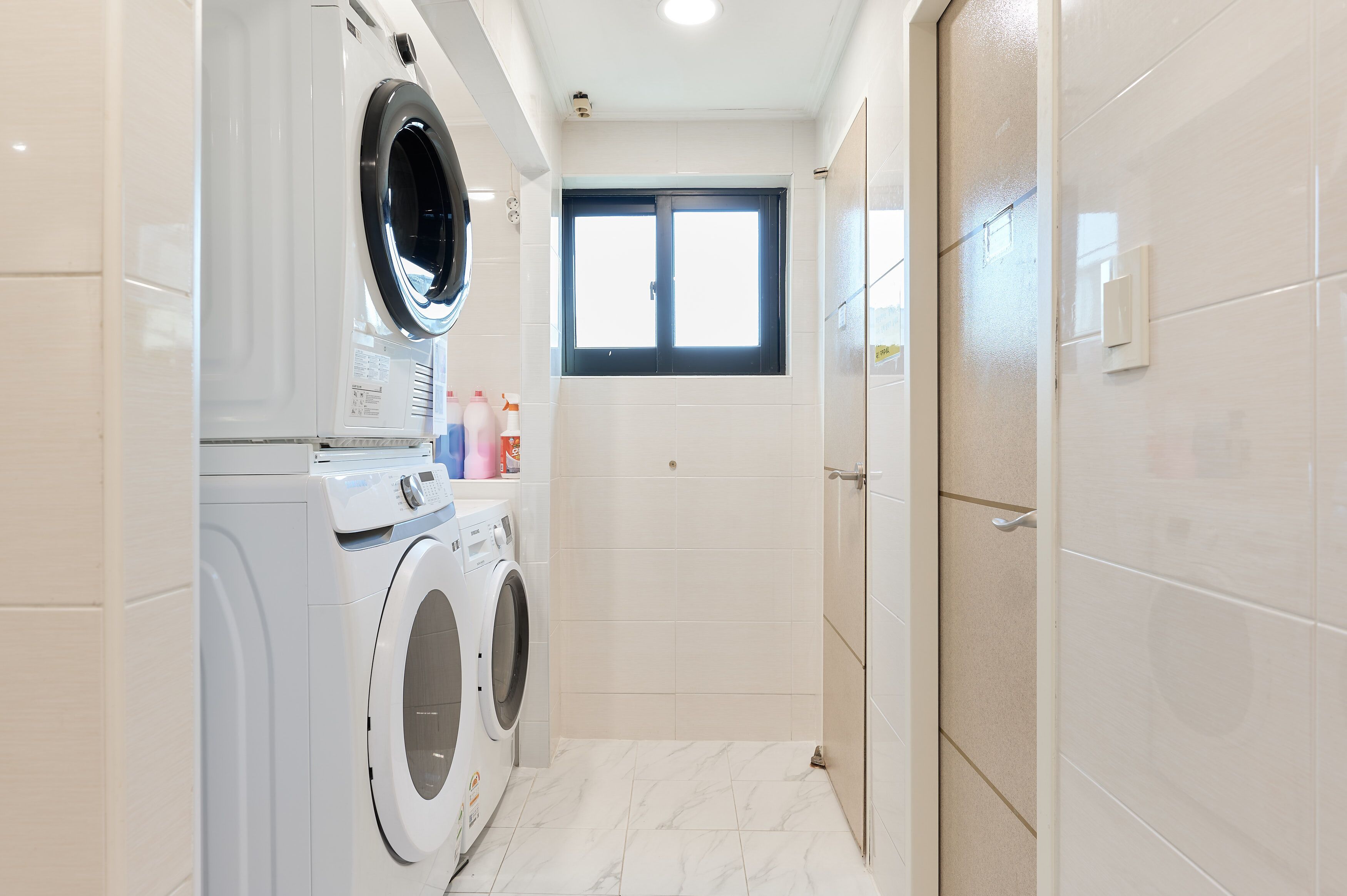 A compact, modern bathroom with a built-in washer and dryer, a small window, and a shower area.