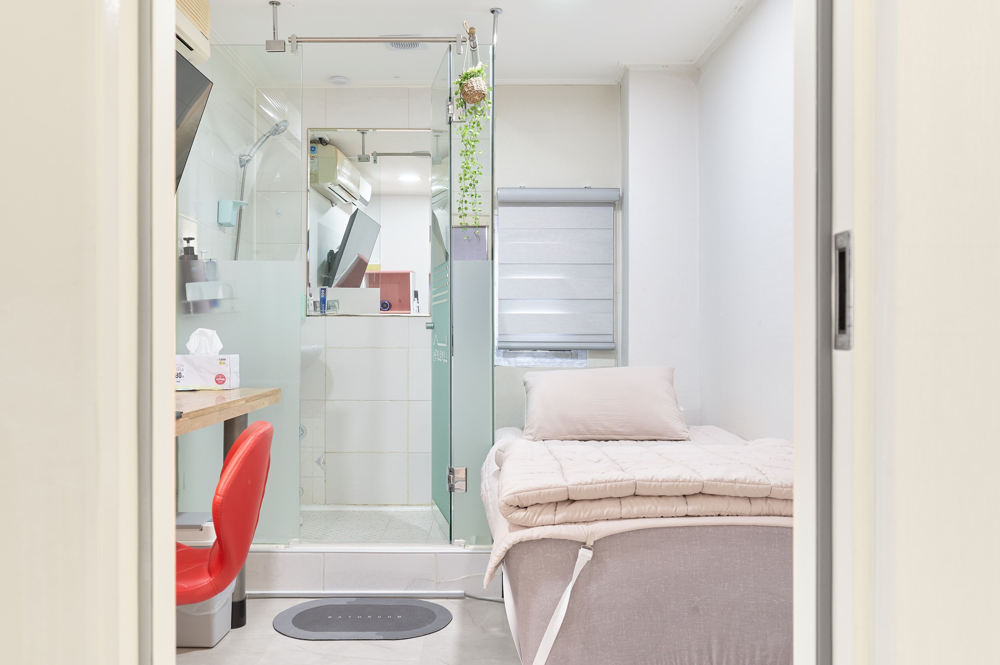 A modern bathroom with a glass shower enclosure, a toilet, and a bed with a white comforter.