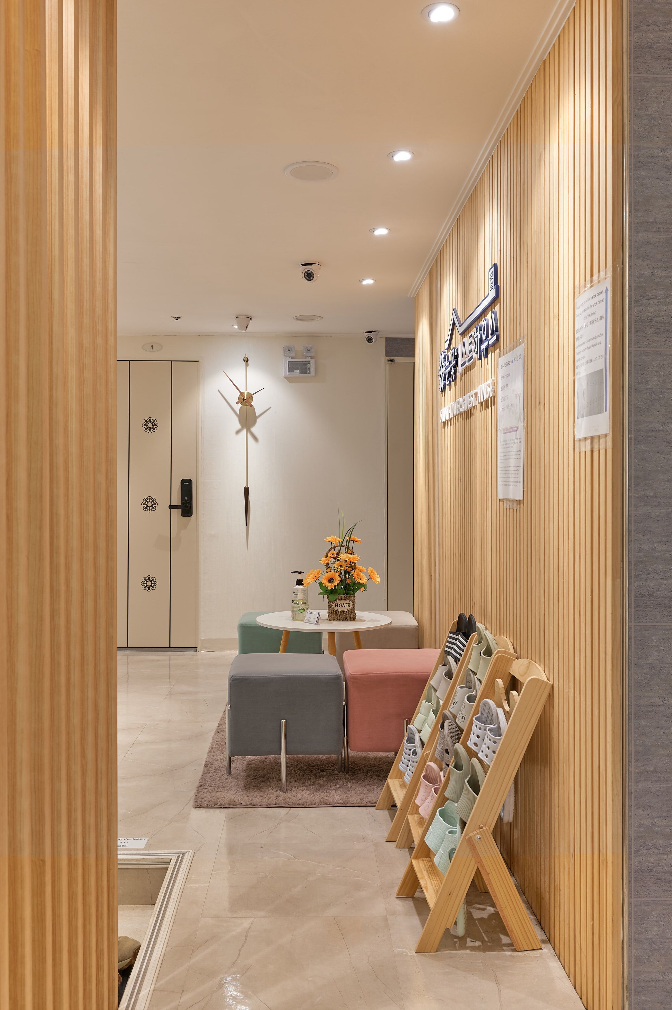 Zona de recepción con pared de madera, mostrador de recepción, cámara montada en la pared y zapatero.