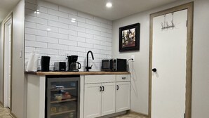 Una cucina compatta con mobili bianchi, un forno a microonde, una macchina per il caffè e un piccolo frigorifero.