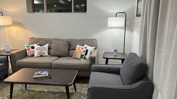 A living room with a sofa, armchair, coffee table, and a lamp.