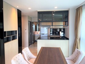 A modern kitchen with a central island, built-in appliances, and a dining area with a wooden table and upholstered chairs. - Deluxe apartment at Panora by Lofty (Choeng Thale)
