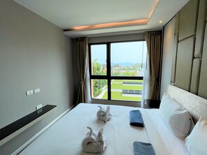 A hotel room with a large bed, a view of a green landscape, and a window with curtains. - Deluxe apartment at Panora by Lofty (Choeng Thale)