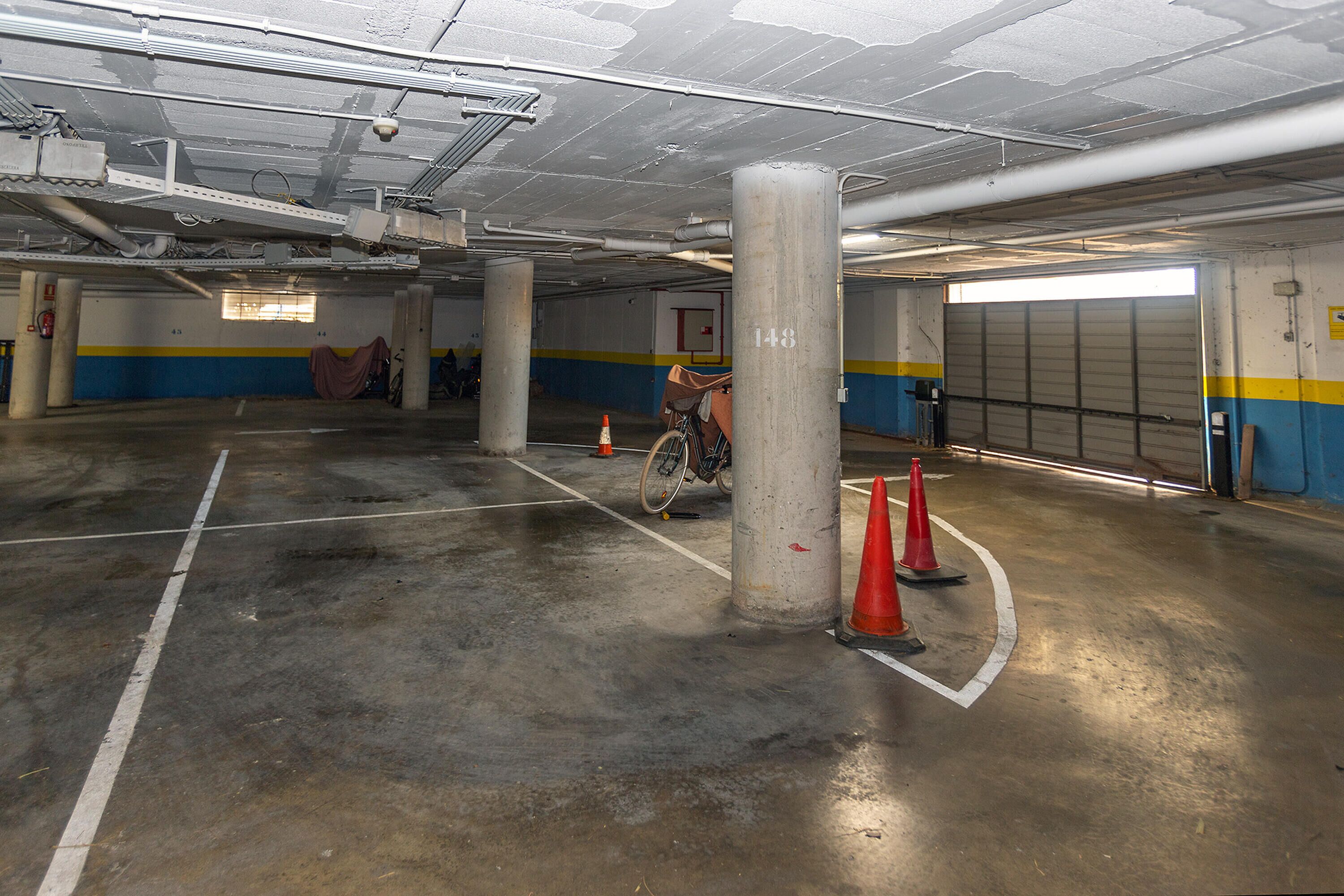 An indoor parking garage with concrete pillars, marked parking spaces, and a bicycle parked near a pillar.