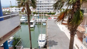 A marina with boats docked, a pedestrian walkway, and palm trees. - Welcome to the charming apartment for rent in Roses, Costa Brava! 1500 meters from the beach, modern accommodation with canal views, sleeps 4. (Roses)