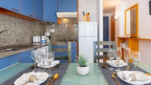 A dining area with a glass table set for two, a small potted plant, and a kitchen in the background. - Welcome to the charming apartment for rent in Roses, Costa Brava! 1500 meters from the beach, modern accommodation with canal views, sleeps 4. (Roses)