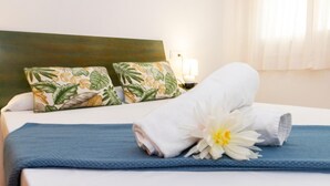 A neatly made bed with a blue bedspread, two pillows with a tropical leaf pattern, and a white towel with a white flower. - Welcome to the charming apartment for rent in Roses, Costa Brava! 1500 meters from the beach, modern accommodation with canal views, sleeps 4. (Roses)