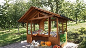 Ein hölzernes Gebäude mit geneigtem Dach, umgeben von Gras und Bäumen, mit einer Präsentation von Obst und Gemüse.