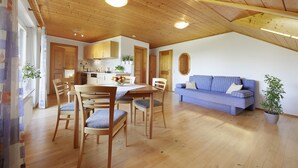 Eine Holzbalkendecke, ein Esstisch mit Stühlen, eine Couch und ein Blumentopf.