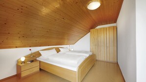 Ein Schlafzimmer mit schrägem Dach, einem hölzernen Bett, einem Nachttisch mit Lampe und einem Kleiderschrank.