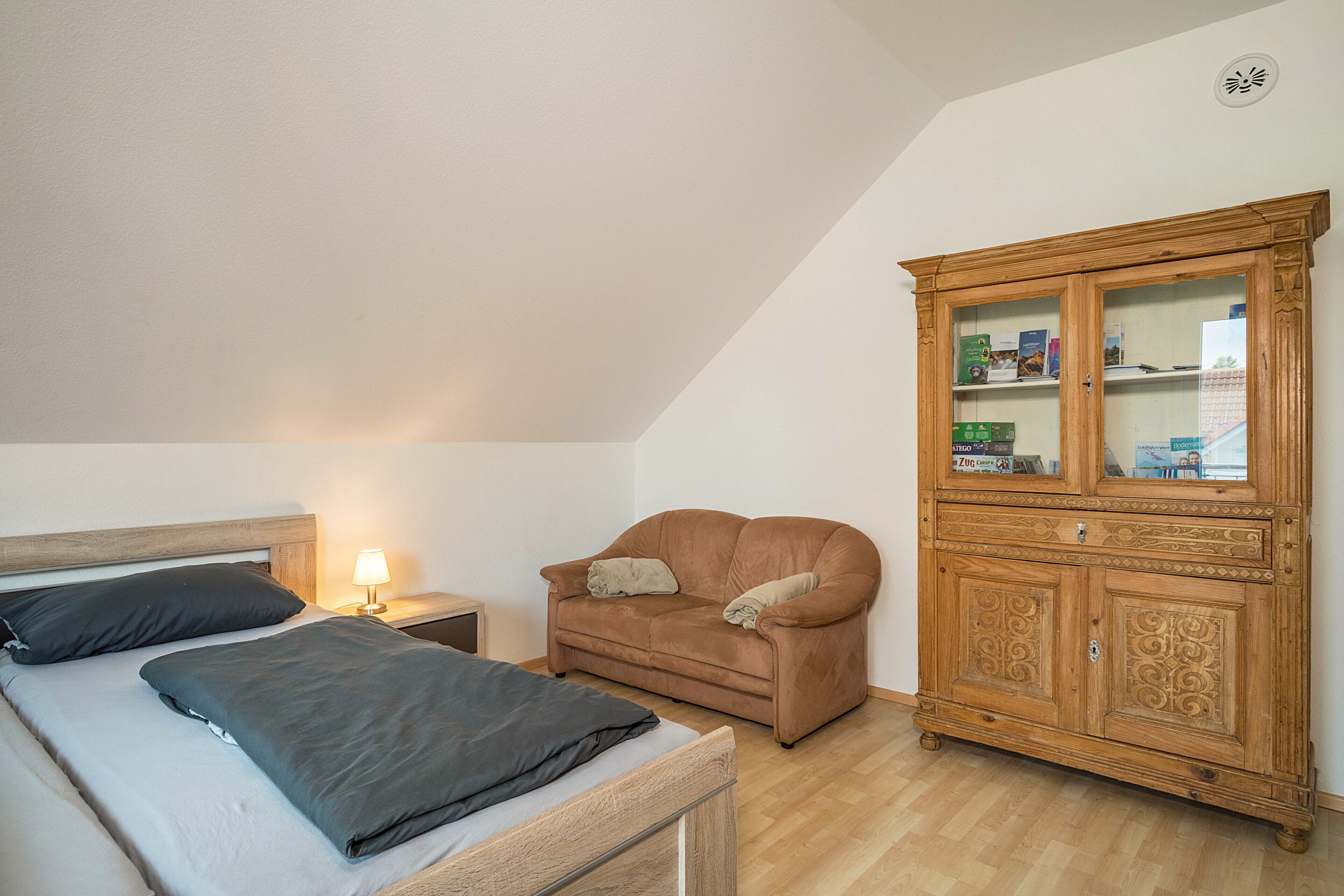 A bedroom with a bed, a nightstand, a brown sofa, and a wooden cabinet with glass doors.