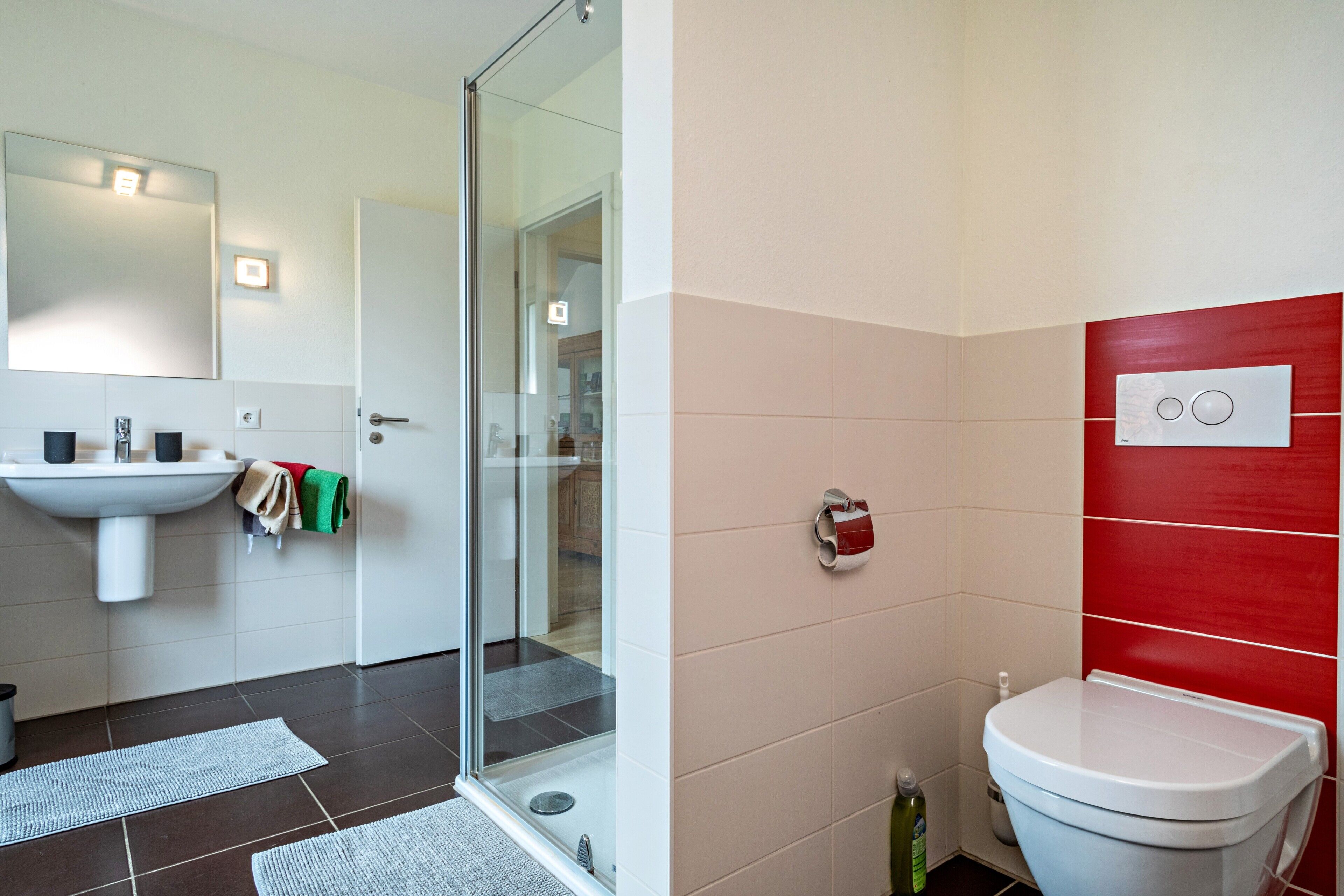 Une salle de bain avec une douche à parois de verre, un lavabo blanc et un mur recouvert de carreaux rouges.