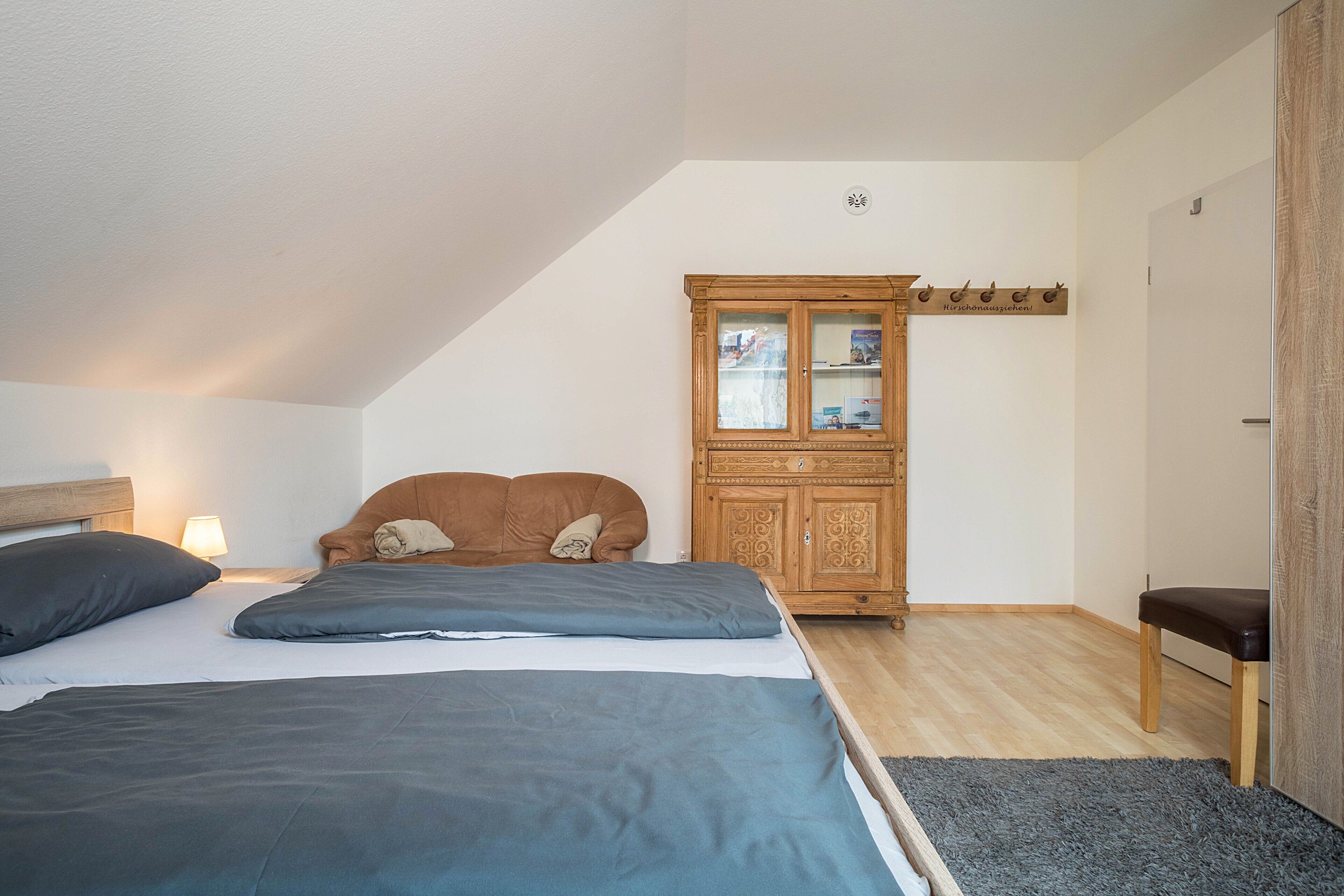 Ein Schlafzimmer mit zwei Betten, einem Holzschrank, einer Bank und einem Wandhaken für Kleidung.