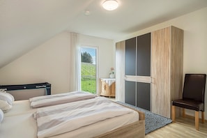 A bedroom with a bed, a chair, a wardrobe, and a view of greenery outside. - Holiday Apartment "Haus Barbara, 90 qm' with Private Terrace & Wi-Fi (Lindau am Bodensee)