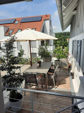 A balcony with a table, chairs, potted plants, and a white umbrella. - Holiday Home 'Kleines Landhaus Bodensee' with Lake View, Balcony & Wi-Fi (Überlingen)