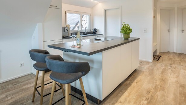 Une cuisine moderne avec un îlot central, des tabourets de bar et une plante en pot.