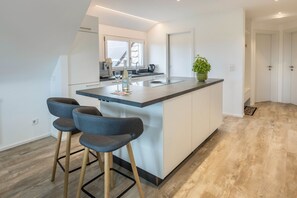 Une cuisine moderne avec un îlot central, des tabourets de bar et une plante en pot.