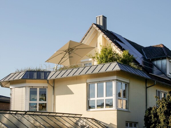 Una casa moderna con techo inclinado, paneles solares y un gran paraguas.
