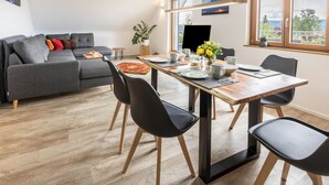 Un salon moderne avec un canapé gris, une table à manger, des chaises et un téléviseur.