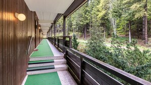 Ein Korridor mit Holzwänden, einem pflegeleicht bepflanzten Weg und einem Geländer mit Blick auf eine bewaldete Landschaft.