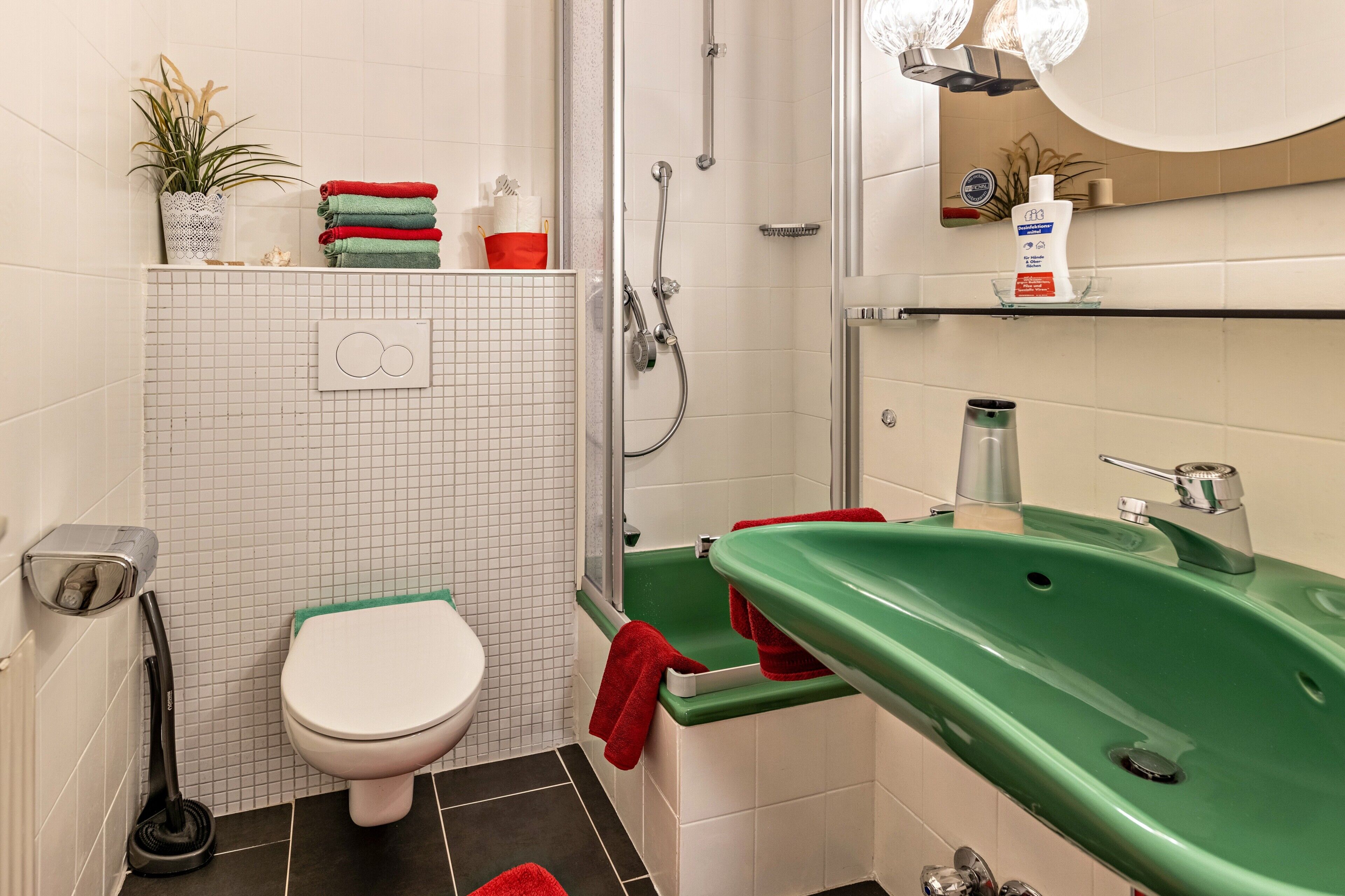 Un baño con inodoro, un lavabo verde, ducha y una planta en maceta.