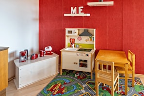 A child's playroom with a kitchen play area, a wooden table, and a colorful rug.