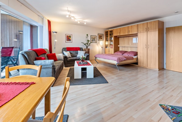 A modern living room with a sofa, a dining table, a coffee table, and a bed with a wooden wardrobe.