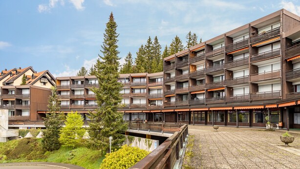 Ein mehrstöckiges Hotel mit Balkonen, Innenhof und umgebender Bepflanzung.