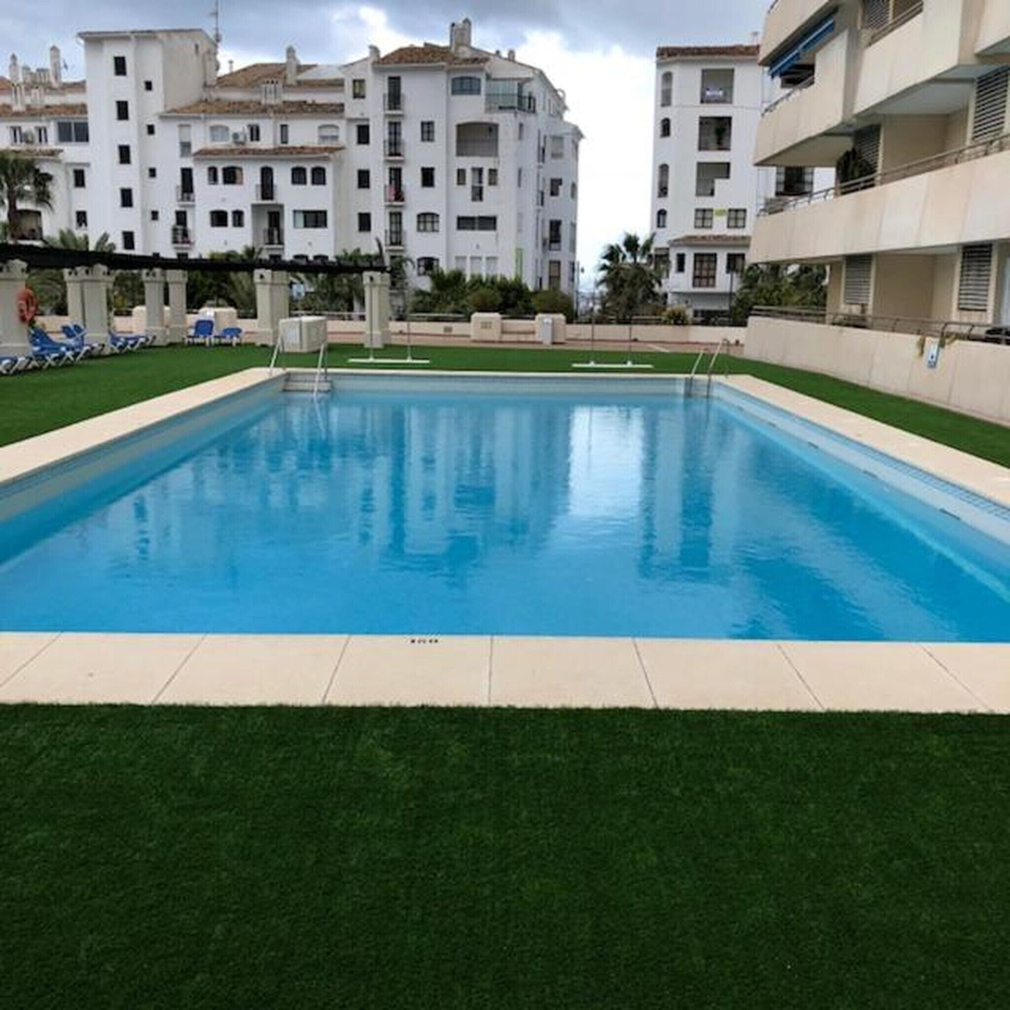 Una piscina rodeada de césped y edificios blancos con balcones.