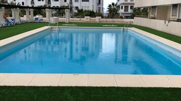 Una piscina rodeada de césped y edificios blancos con balcones.