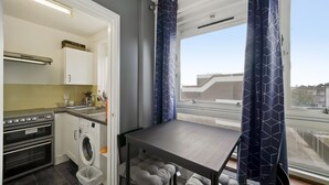 Een kleine keuken met een wasmachine, een tafel en een raam met gordijnen.