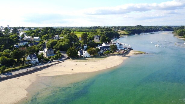 Vista aerea di una zona costiera con spiaggia sabbiosa, un porto turistico con barche e edifici residenziali.