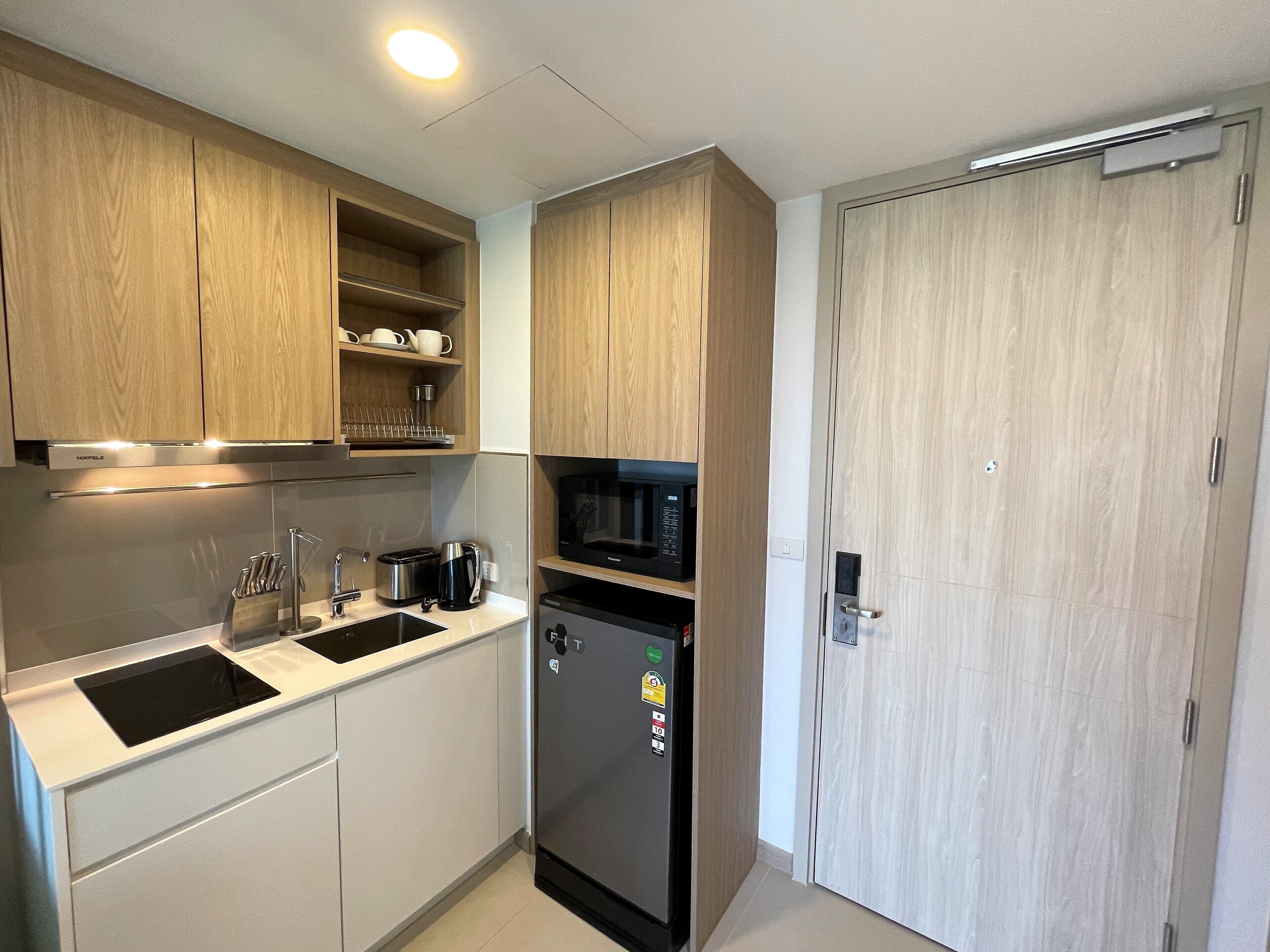 Una cocina moderna con armarios de madera, microondas integrado, refrigerador y un lavamanos con grifo.