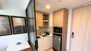 Eine kompakte Küche mit Kühlschrank, Mikrowelle und Spüle. Ein Esstisch mit Stühlen, darüber hängen Holzschränke.