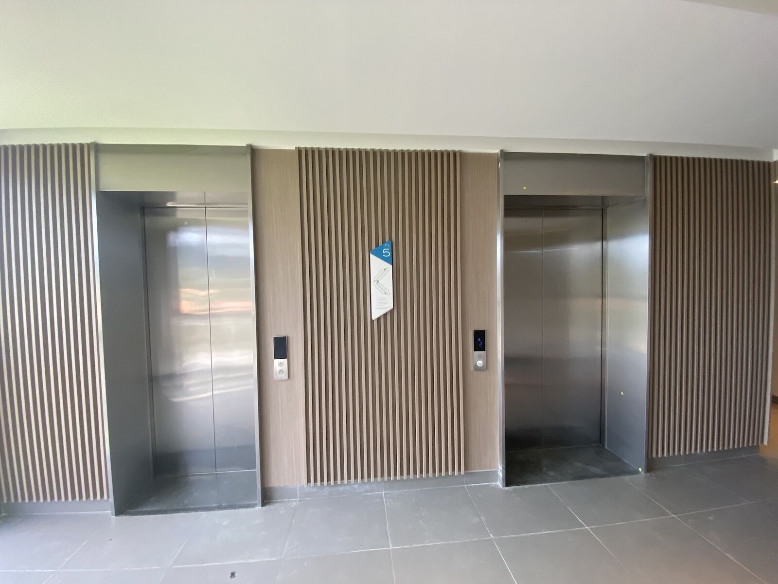 A modern elevator area with three elevators, each with a metallic finish and a control panel.