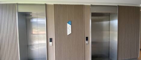Un área de ascensores moderna con tres ascensores, cada uno con acabado metálico y panel de control.