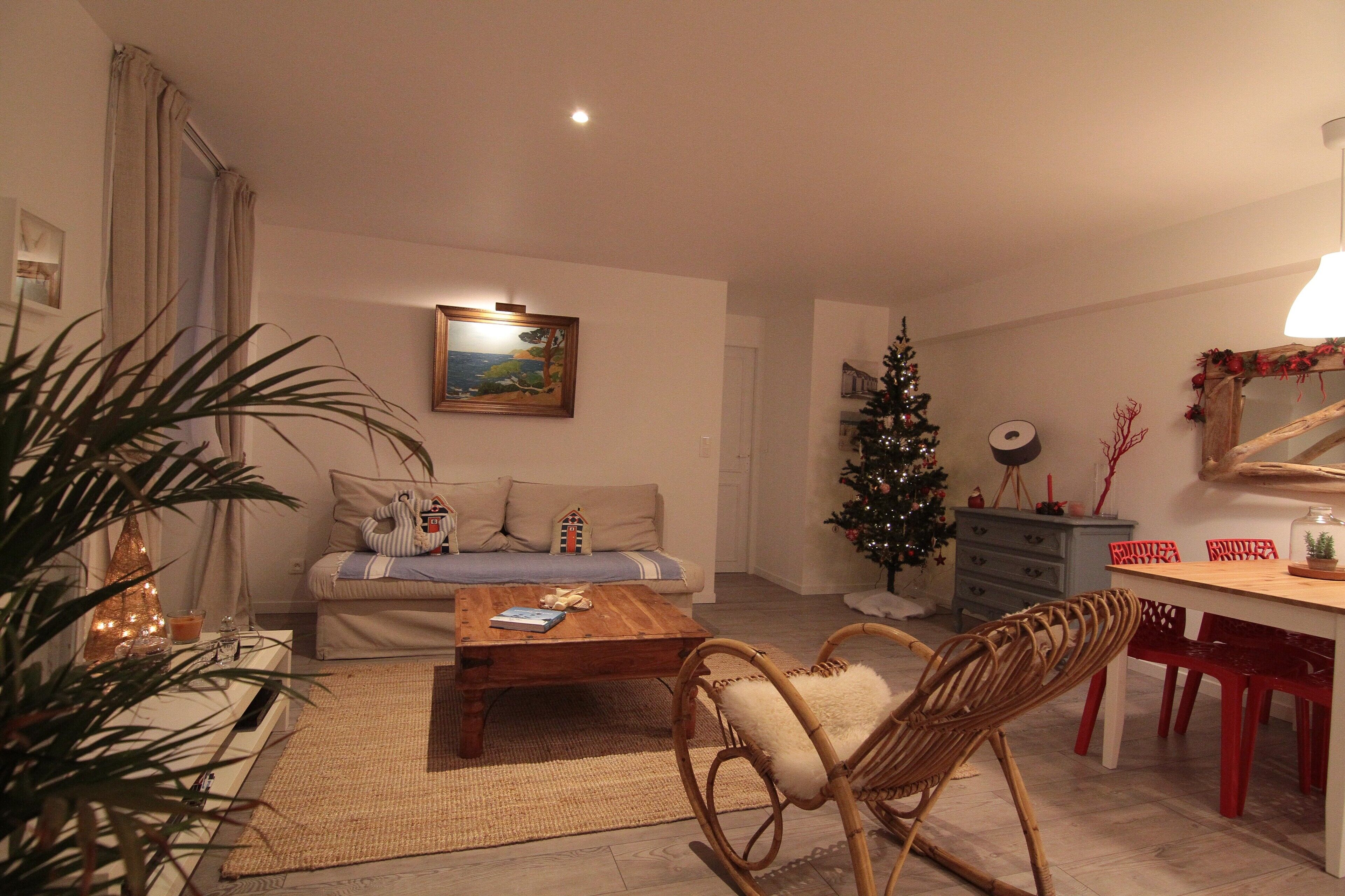 A living room with a sofa, a coffee table, a dining table with chairs, a Christmas tree, and a painting on the wall.