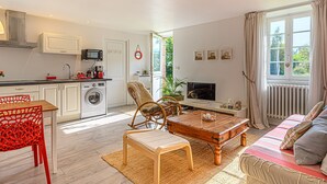 A modern kitchen with a washing machine, a dining area with a red chair, a sofa with a striped blanket, and a TV in the living room.