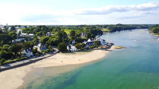 A coastal area with a sandy beach, a row of houses, and a calm river.