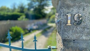 A stone wall with the number 19 engraved on it, a metal gate, and a blurred background of greenery. - Studio 'Villa Prat Bras - Sea View' with Shared Garden and Wi-Fi (Clohars-Carnoët)