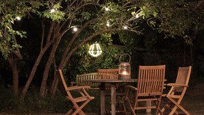 A wooden table and chairs set outdoors at night, surrounded by trees and string lights.