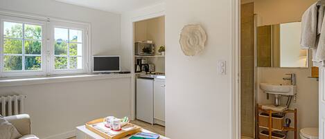 A room with a sofa, a table with a tray and book, a TV, a kitchen area, and a bathroom with a sink and toilet.