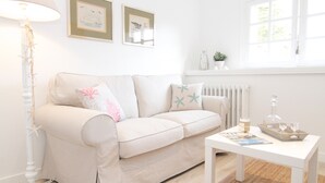 A living room with a sofa, a table, a floor lamp, and framed artwork on the wall.