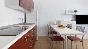 A modern kitchen with a white countertop, stainless steel appliances, and red cabinetry. There is a dining area with a white table and red chairs. A flat-screen TV is mounted on the wall above the dining table.