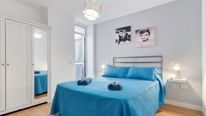 A bedroom with a bed, a wardrobe, a bedside table with a lamp, and two wall-mounted pictures.