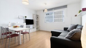 A modern living space with a dining area, a sofa, a TV, and a window with blinds.