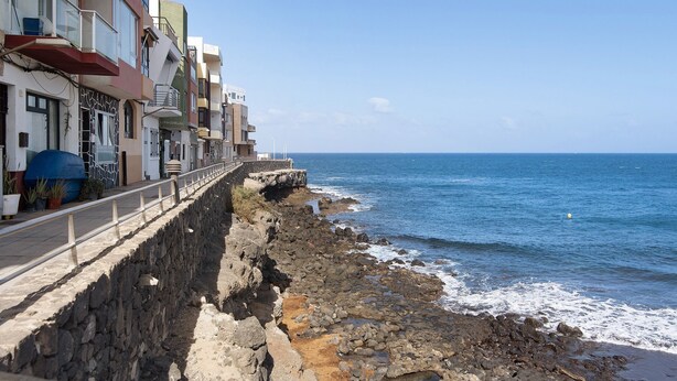 A coastal hotel with a stone retaining wall, balconies, and a view of the sea.