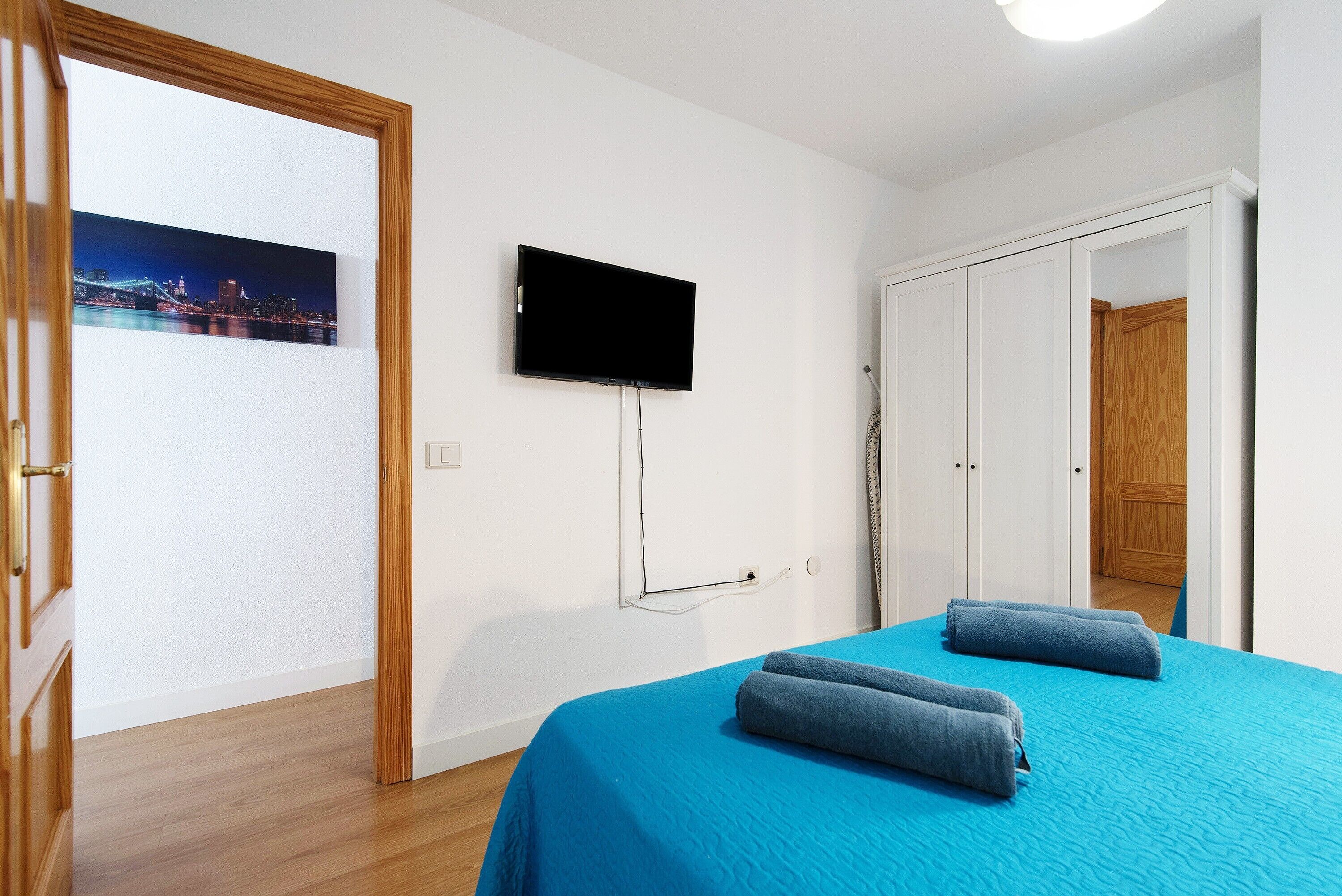 Une chambre à coucher avec un lit, un téléviseur fixé au mur et une porte donnant sur une autre pièce.